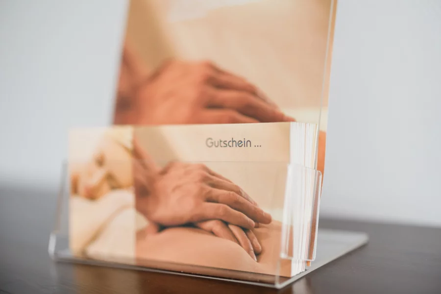 Entspannung verschenken – Massagegutscheine erhältlich Massagegutschein mit entspannendem Motiv auf einem Tischaufsteller