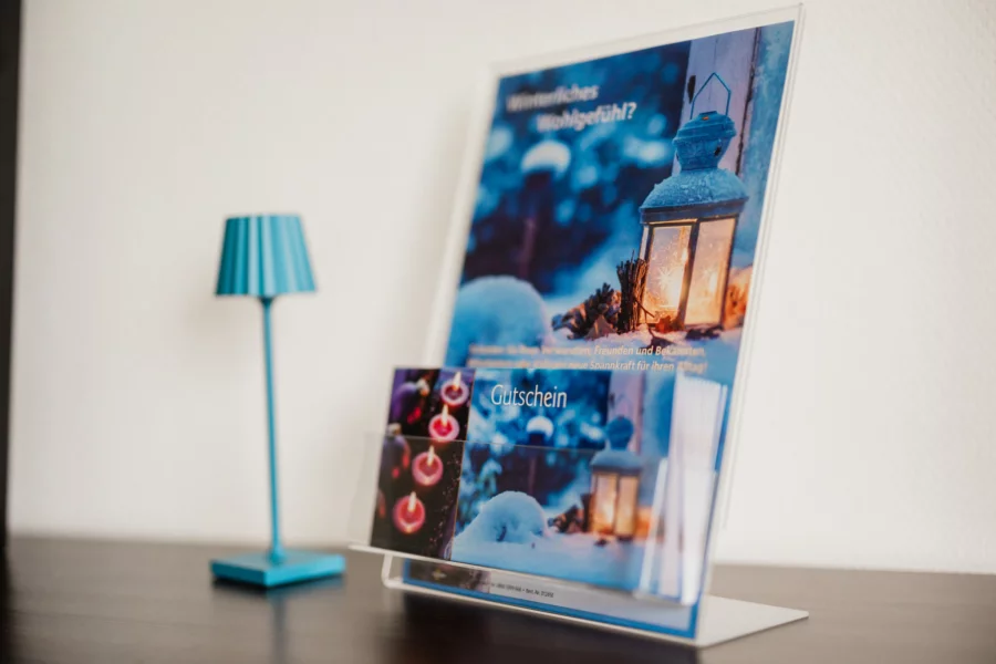 Schenke Wohlbefinden mit einem Massage-Gutschein Massage-Gutschein mit winterlicher Dekoration auf einem Holztisch
